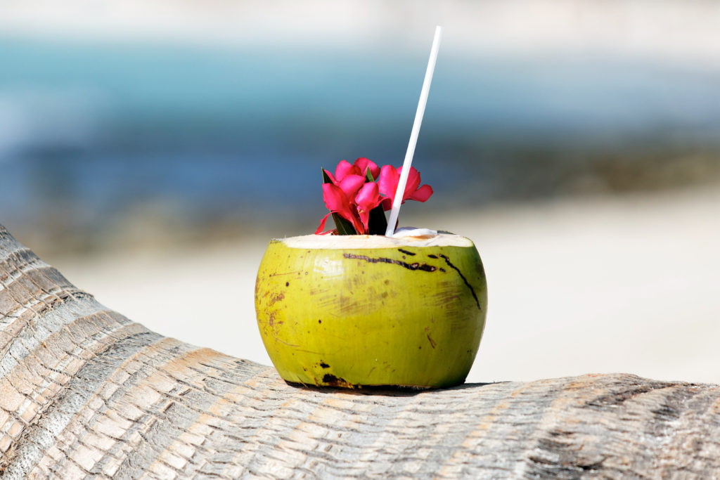 cocktail with drinking straw on palm tree on caribbean beach