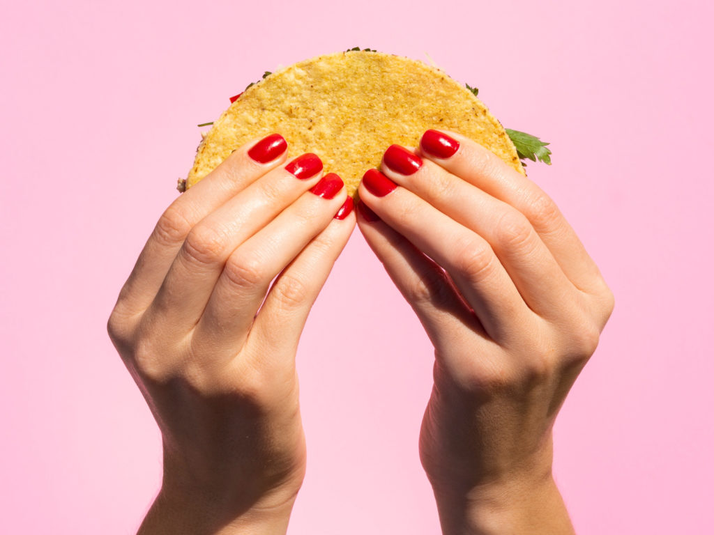 close up hands holding taco with pink background
